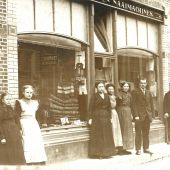 2 naaimeisjes, juffr. Tonia, mevr. Henrika Tielbeek  Holthuis, Bernard Tielbeek en knecht Jan Veldkam voor de winkel in deHerenstraat.jpg